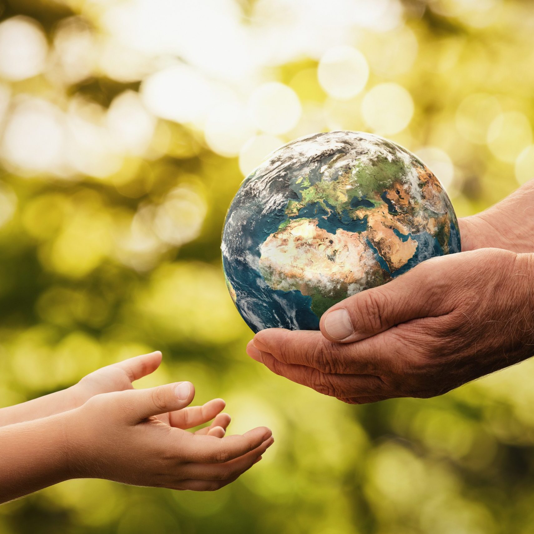 Close up of senior hands giving small planet earth to a child ov Close up of senior hands giving small planet earth to a child over defocused green background with copy space